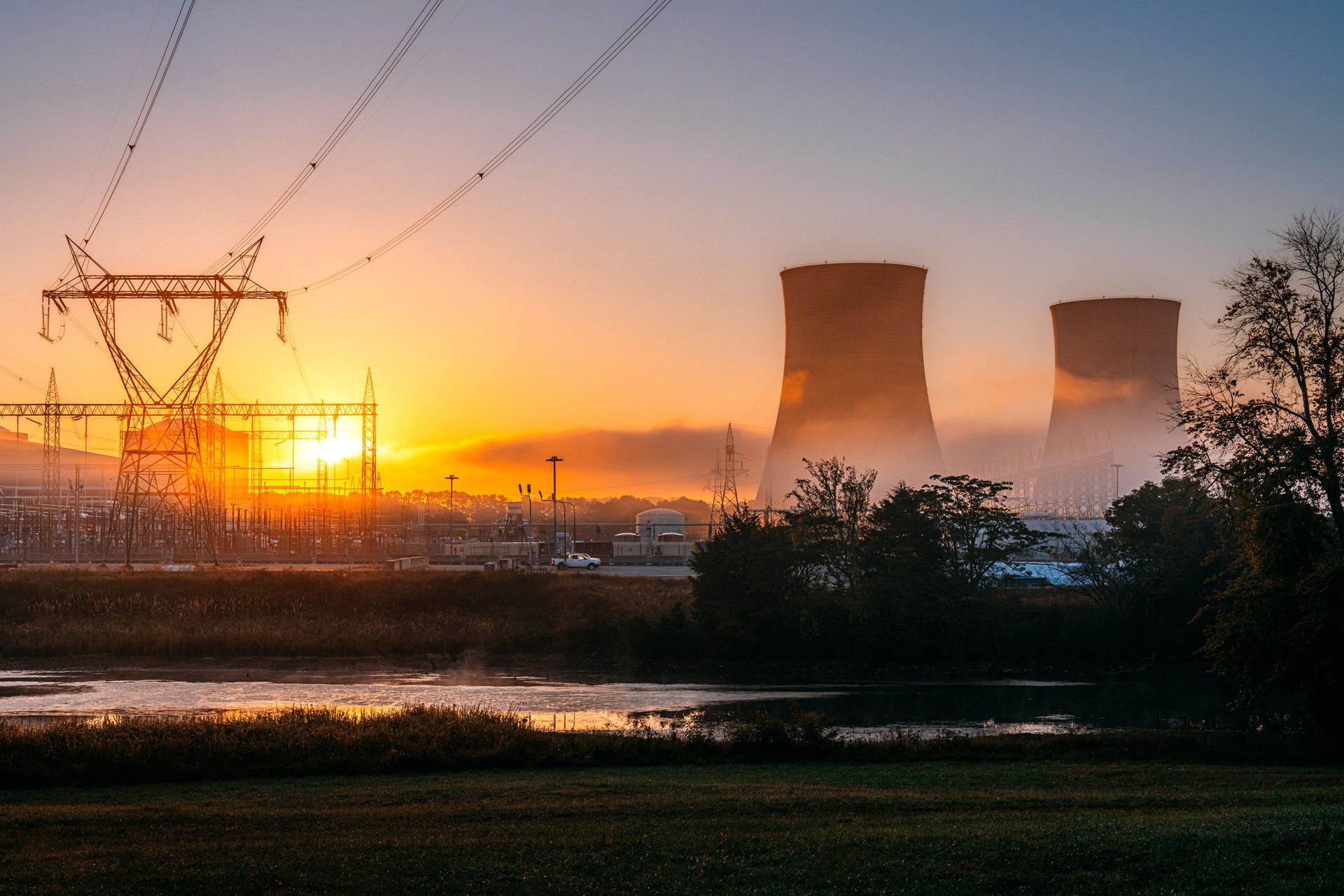 Lever de soleil derrière les tours de refroidissement et les tours en treillis d’une centrale nucléaire